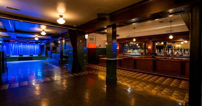 The empty room from the back: dance floor and pillars, the bar on the right and the stage behind a blue curtain