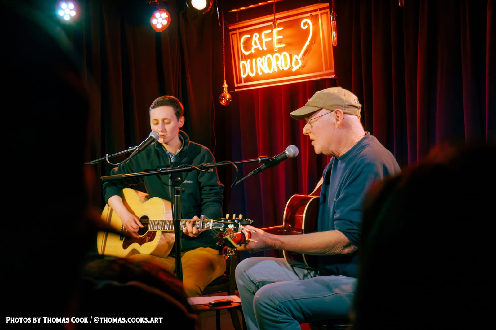 A seated acoustic duo under the neon sign