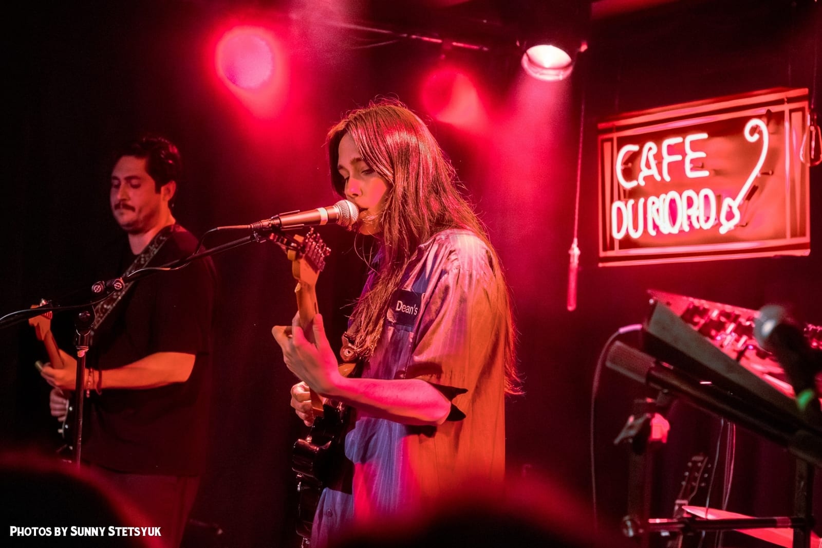 A singer and a guitarist under the red neon sign