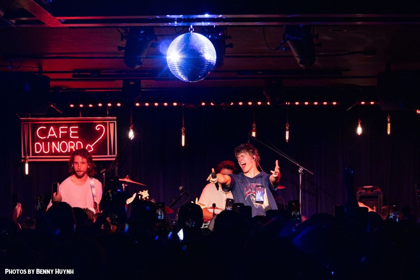 A band on stage under the neon sign and a disco ball, with the crowd in front